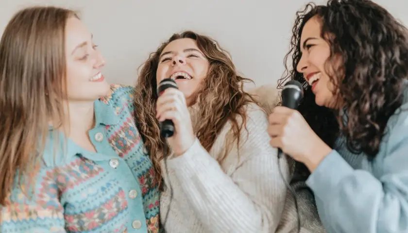 Tre amiche ridono e cantano con microfoni, un momento di gioia con canzoni facili da cantare.