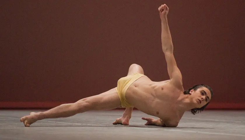 Un ballerino esegue un complesso floor work, con un braccio teso verso l'alto e una gamba distesa.