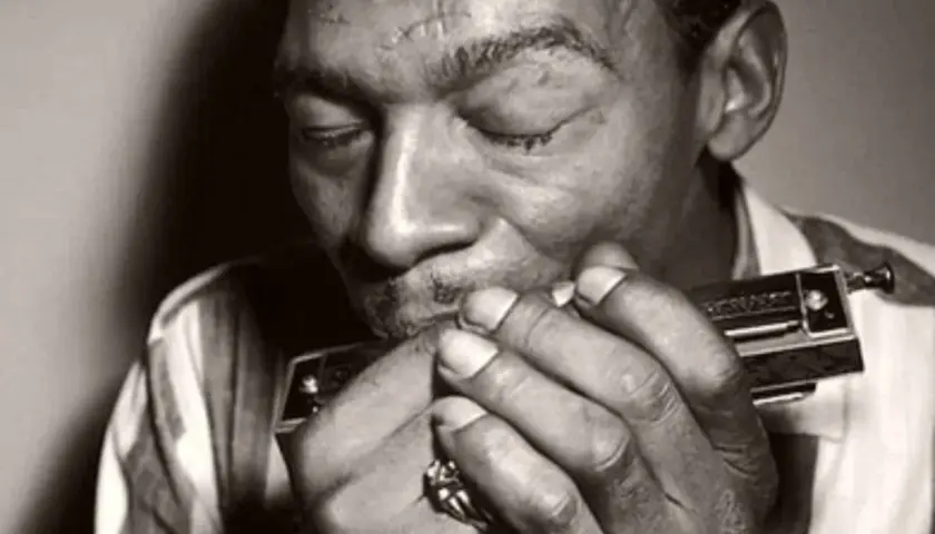L'uomo con l'armonica chiude gli occhi, immerso nella melodia blues che esce dallo strumento.