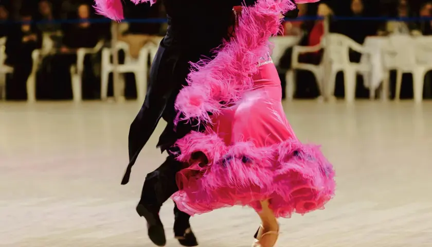 Coppia di ballerini in un vivace fox trot. La donna indossa un abito rosa con piume, l'uomo un completo nero.