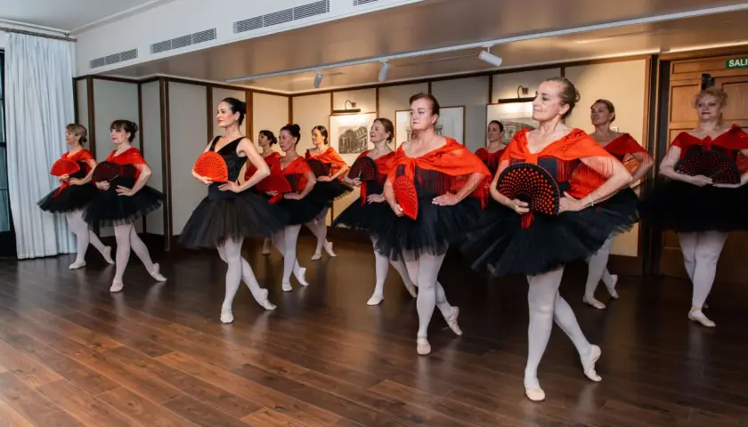 Un gruppo di ballerine con tutù neri e scialli rossi, che tengono ventagli, dimostra cos'è la danza classica con grazia ed eleganza.