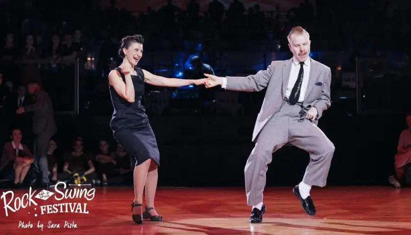 Coppia in abito elegante e vestito scuro si diverte in un energico ballo boogie woogie sul palco di un festival.