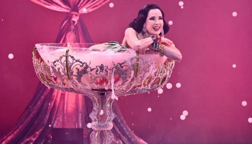 Attrice in un bicchiere gigante, un'esibizione di burlesque dance con schiuma rosa e drappeggi di seta.