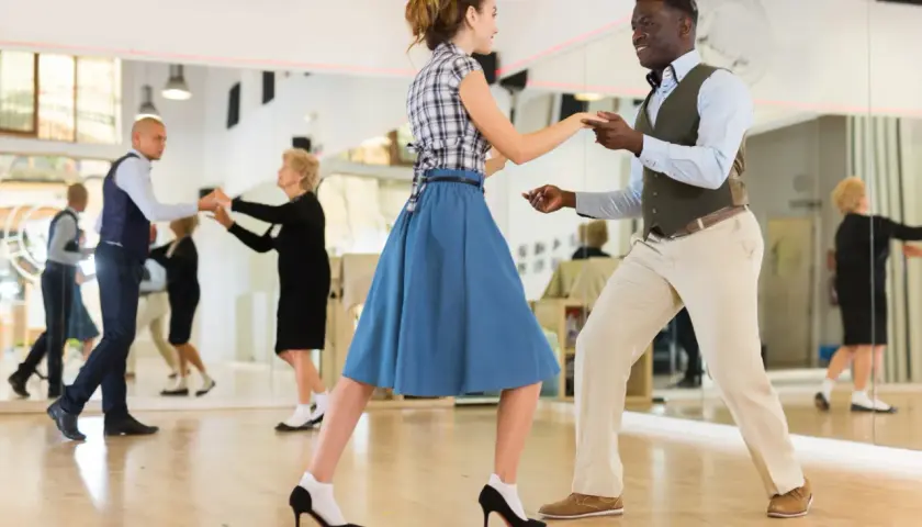 Coppia balla swing in una scuola di ballo. Altri ballerini si esercitano nello specchio.