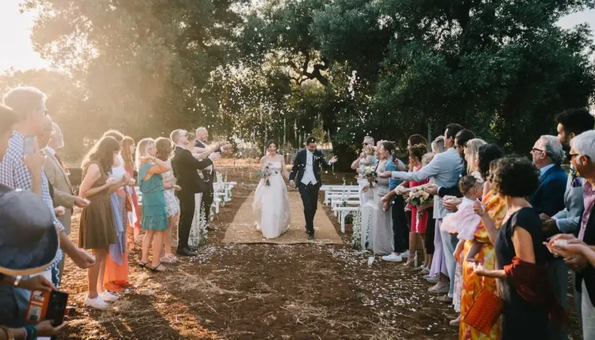 Sposi camminano su un tappeto, circondati da invitati che lanciano petali. La luce del tramonto crea un'atmosfera magica, perfetta per una canzone matrimonio.