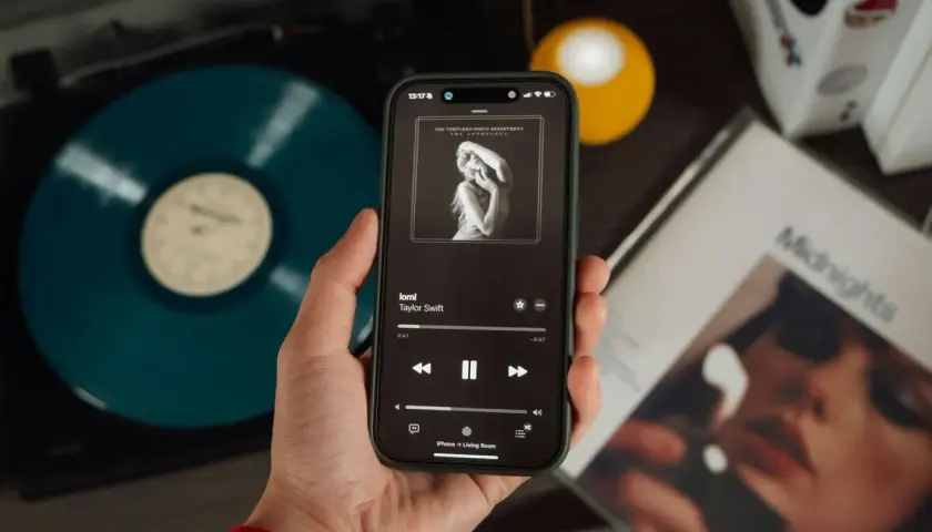 Mano che tiene uno smartphone con la copertina di un album di Taylor Swift. Accanto, un vinile blu e la copertina di "Midnights". Nonostante l'atmosfera moderna, si percepisce il fascino delle canzoni sudamericane.
