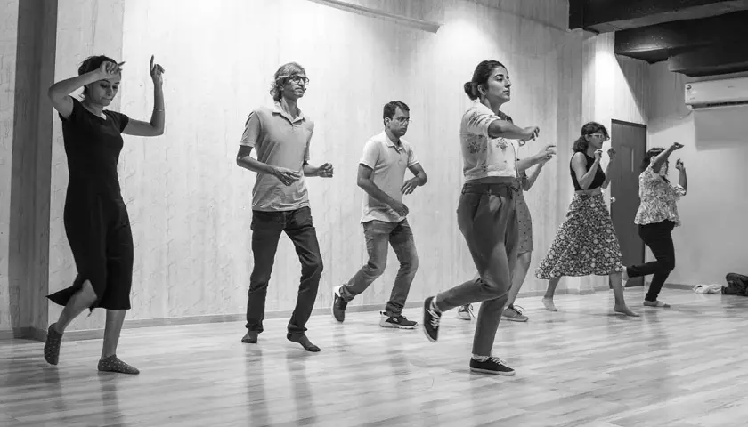 Un gruppo di persone impara come si balla lo swing in una sala prove. Movimenti energici e sorrisi contagiosi.