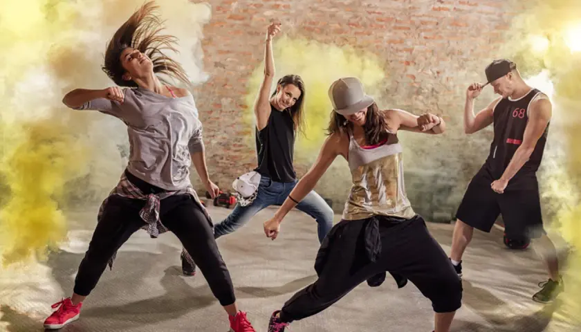 Un gruppo di ballerini energici in un ambiente urbano, circondati da fumo giallo. Un esempio di video dance cos'è: pura espressione e movimento.