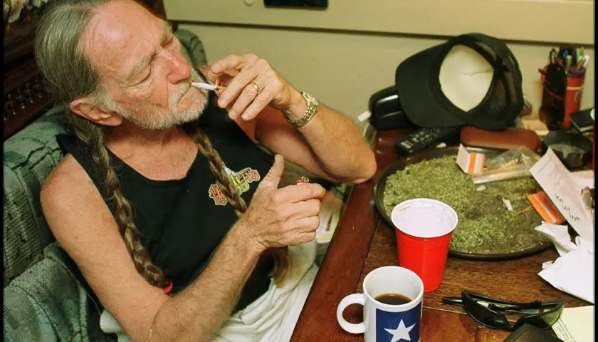 Willie Nelson, icona delle migliori canzoni country americane, accende una sigaretta con una tazza di caffè accanto.