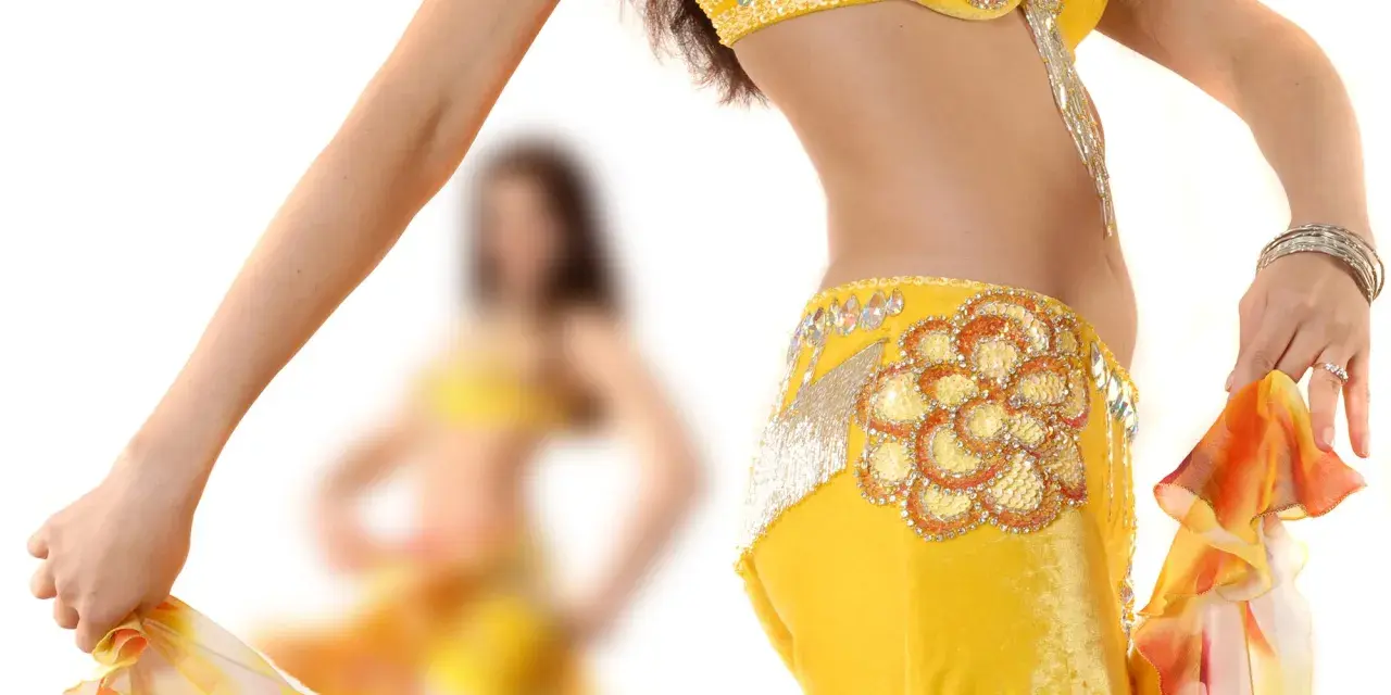 Dettaglio di una ballerina che esegue una danza del ventre, con abito giallo decorato e velo colorato.