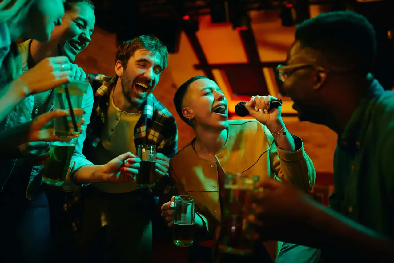Amici che cantano a squarciagola, bevendo e divertendosi con duetti karaoke facili in un locale illuminato da luci colorate.