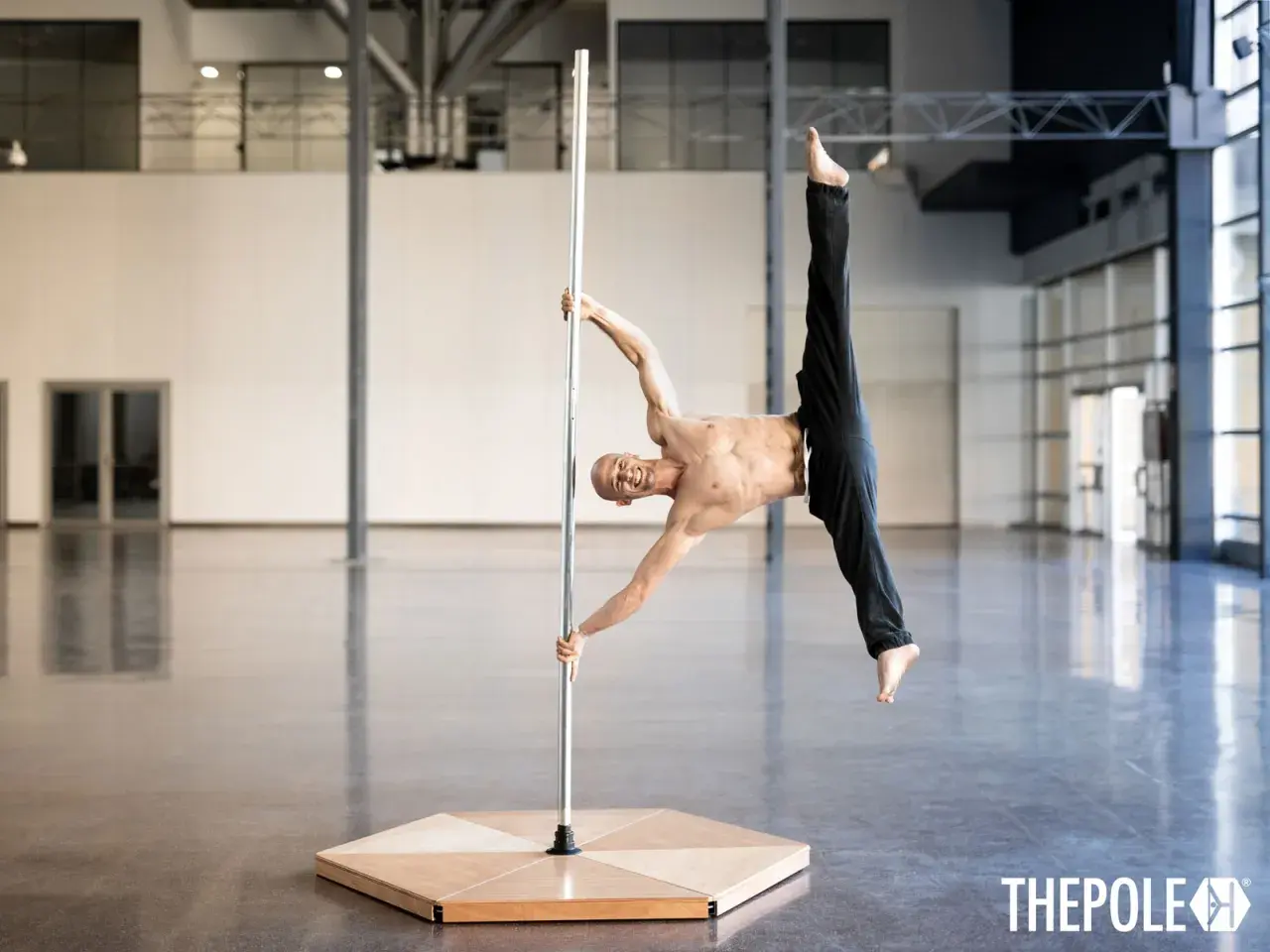 Uomo in posa acrobatica su un palo, dimostra che anche i pole dance principianti possono raggiungere incredibili posizioni con la giusta dedizione.