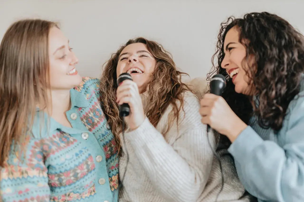Tre amiche ridono e cantano con microfoni, un momento di gioia con canzoni facili da cantare.