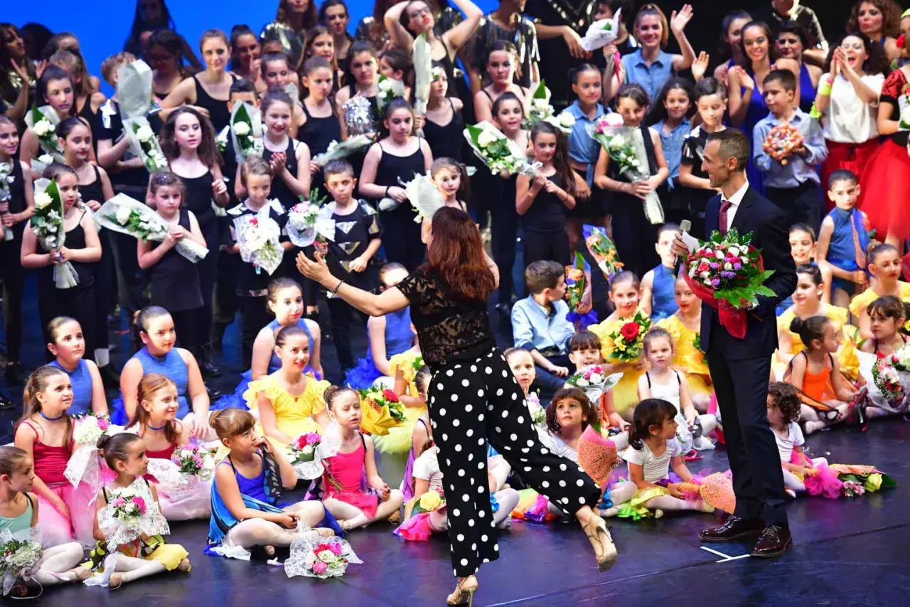 Giovani ballerini festeggiano sul palco dopo un'esibizione di rumba ballo latino americano, ricevendo fiori e applausi.