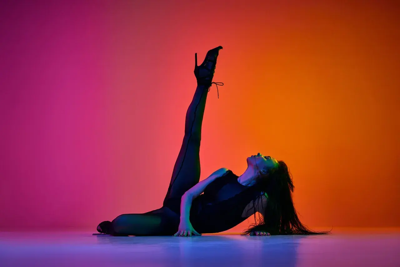 Danza sensuale con tacchi alti, una ballerina si piega all'indietro su uno sfondo sfumato di rosa e arancione.
