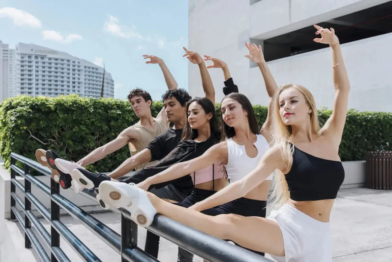 Giovani ballerini in una lezione di danza all'aperto, con un edificio moderno e vegetazione sullo sfondo.
