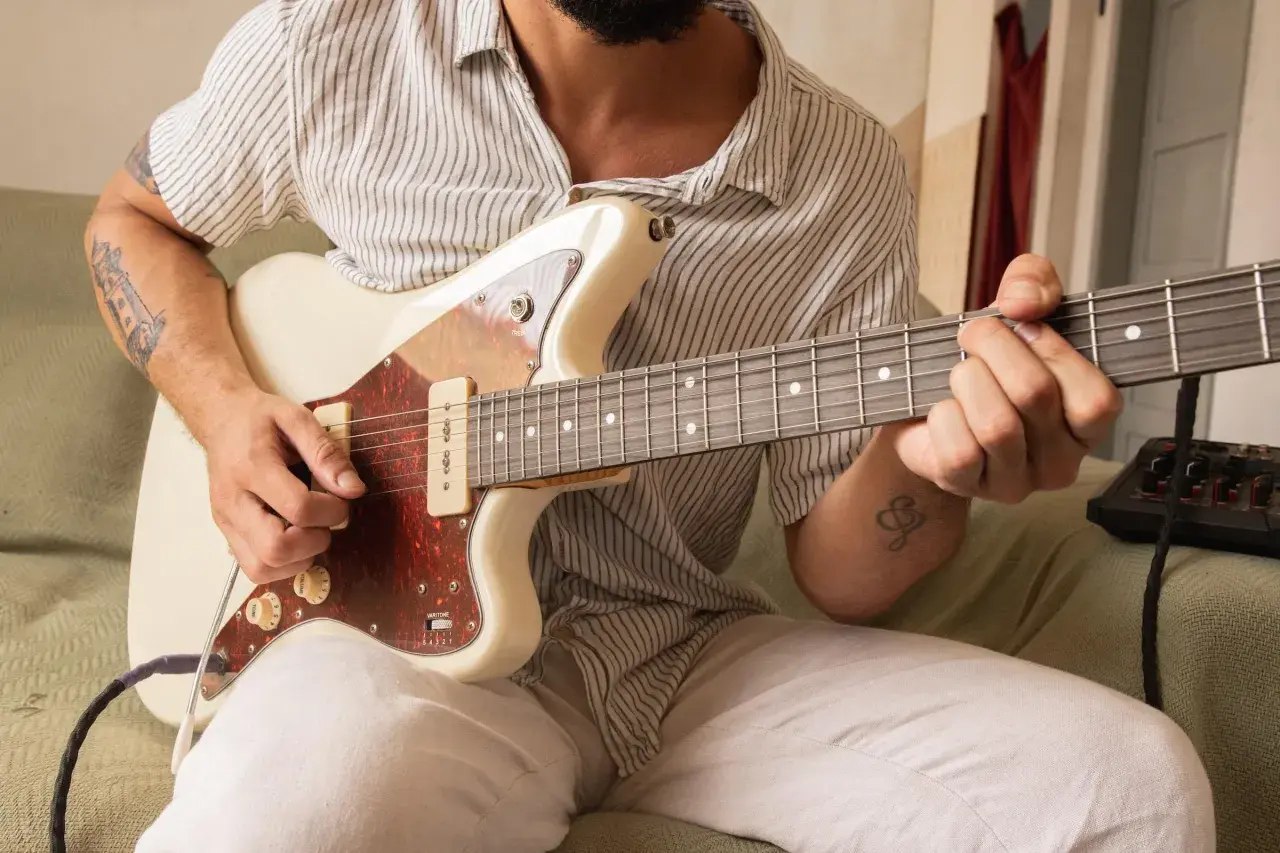 Un chitarrista con tatuaggi si prepara a suonare, concentrato su come accordare la chitarra.