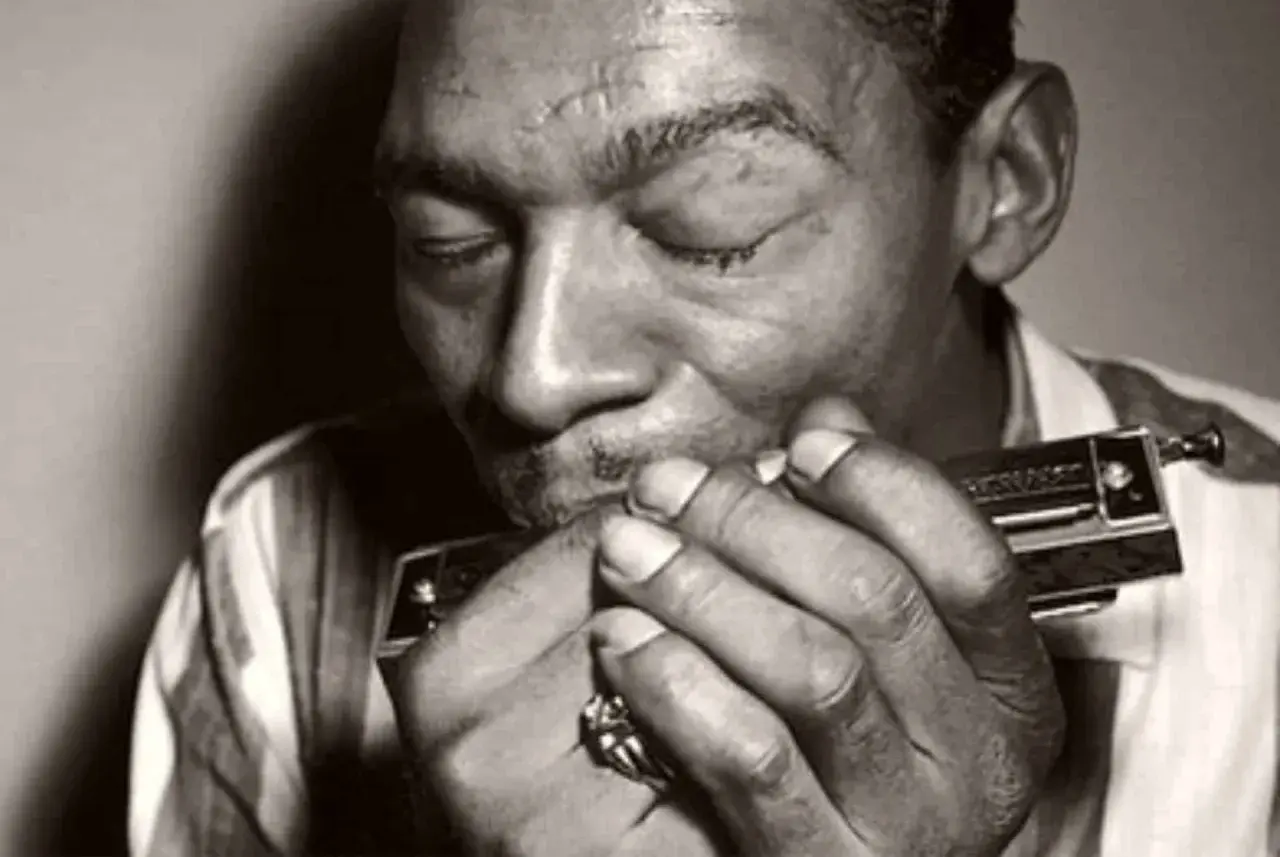 L'uomo con l'armonica chiude gli occhi, immerso nella melodia blues che esce dallo strumento.
