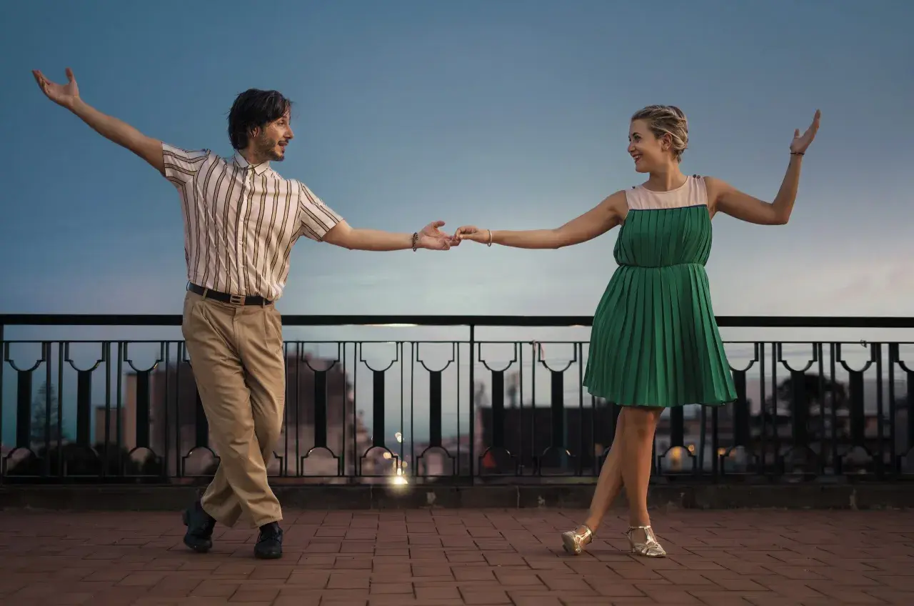 Coppia balla con gioia, un uomo e una donna in abiti retrò, mostrando cos'è lo swing con movimenti aggraziati al tramonto.