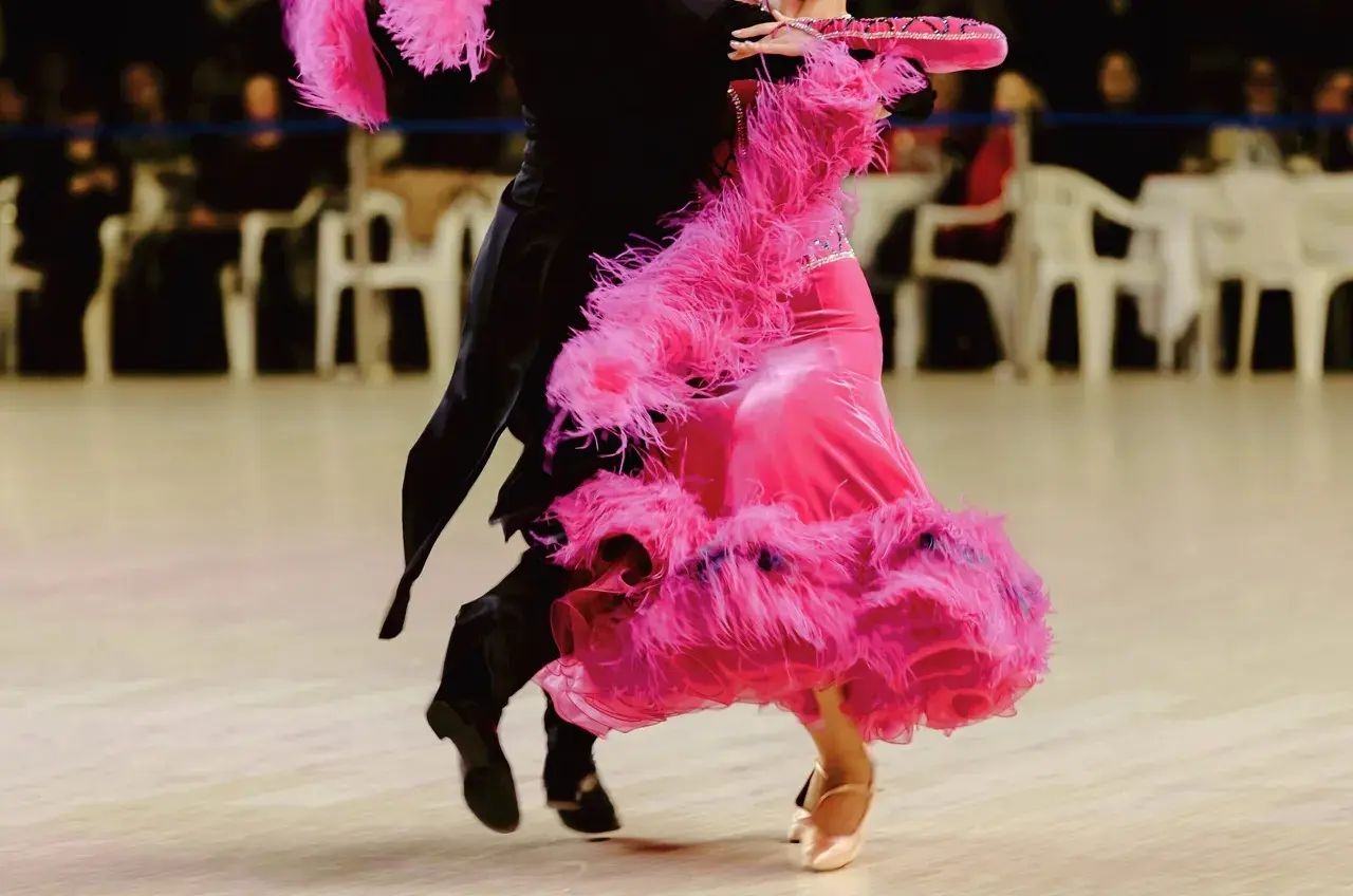 Coppia di ballerini in un vivace fox trot. La donna indossa un abito rosa con piume, l'uomo un completo nero.