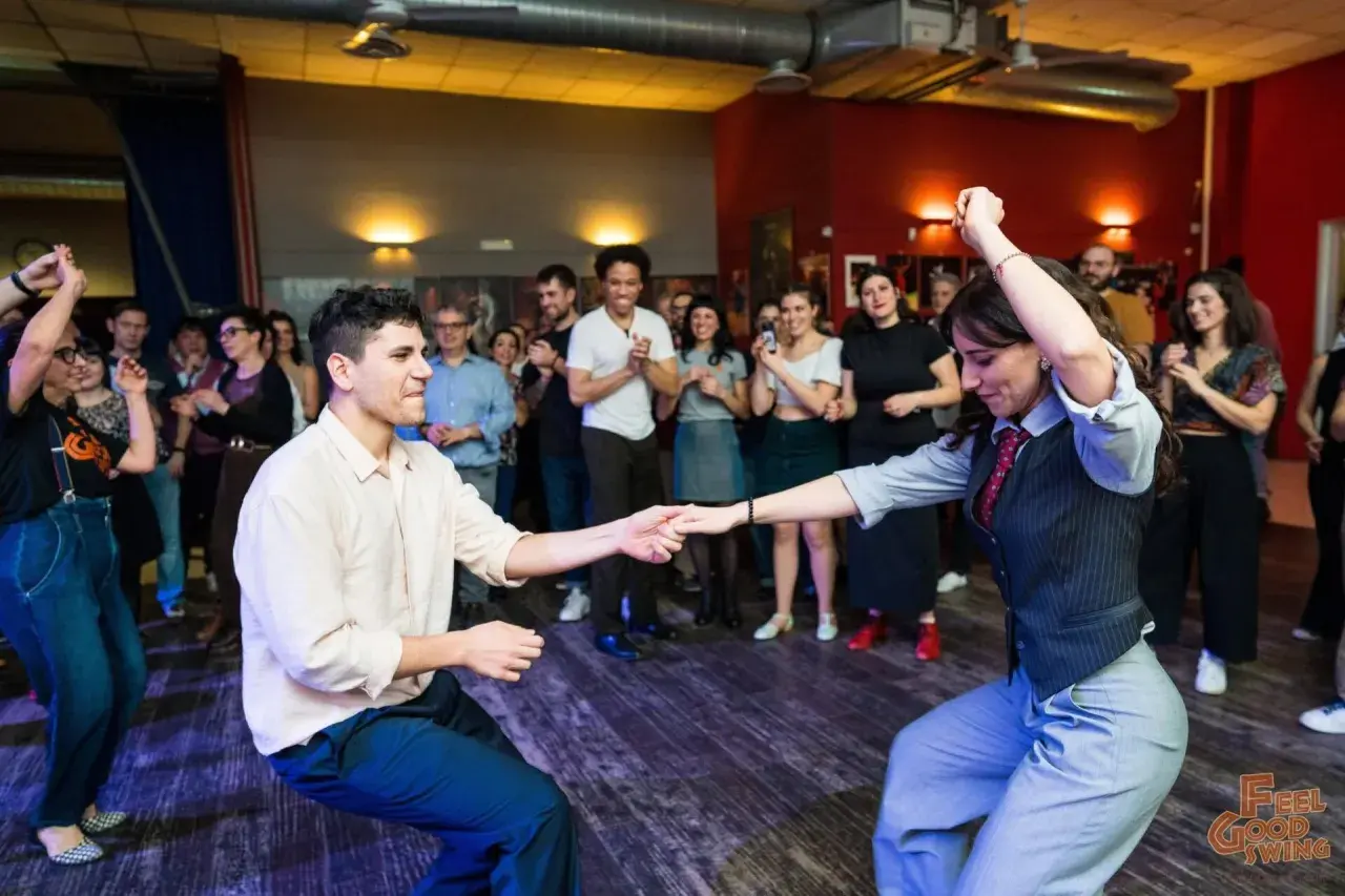Coppia in movimento durante lezioni di ballo per principianti, con spettatori che osservano.