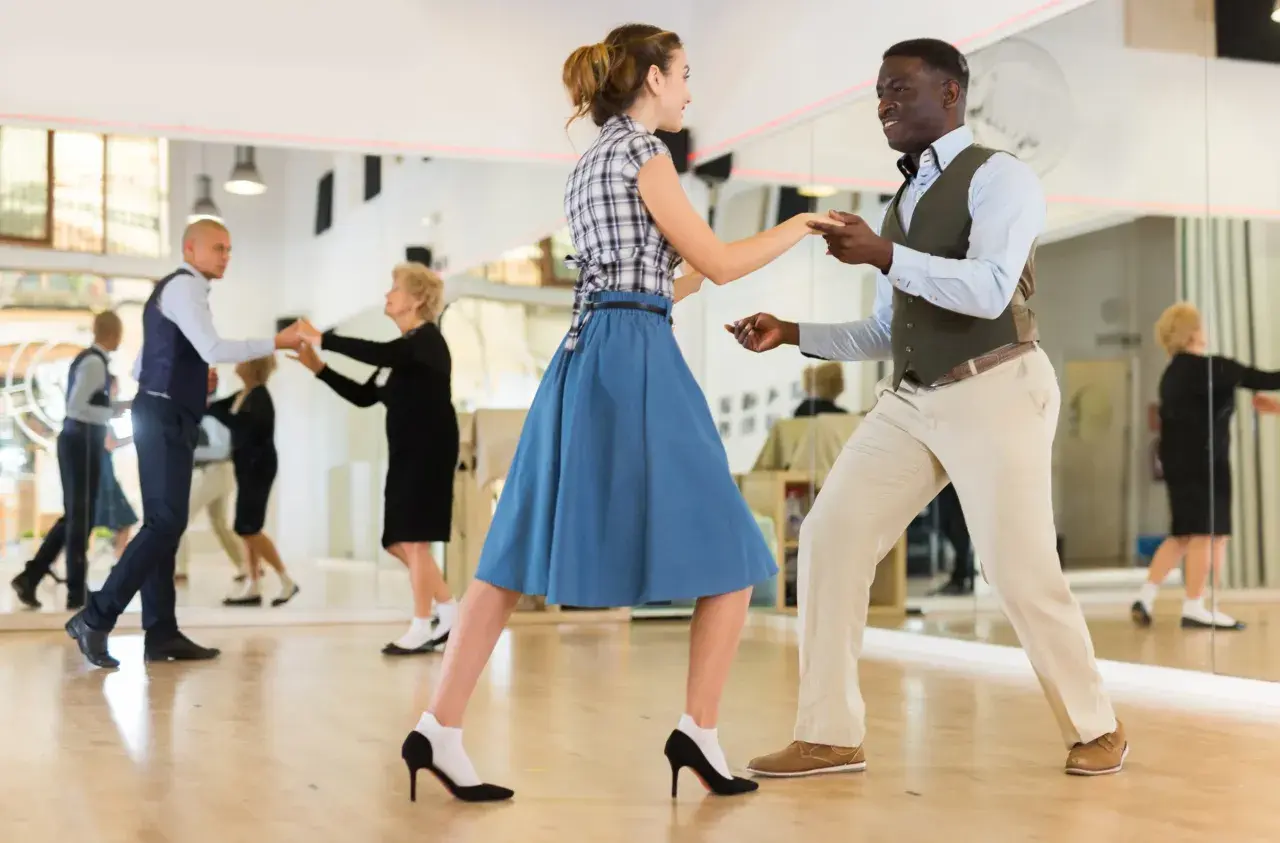 Coppia balla swing in una scuola di ballo. Altri ballerini si esercitano nello specchio.
