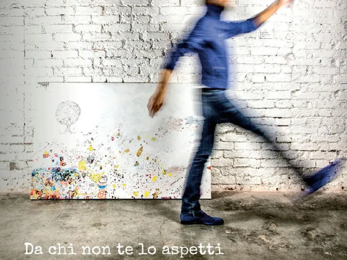 A blurred figure in blue jeans and a jacket walks past a canvas covered in colorful abstract art and doodles.