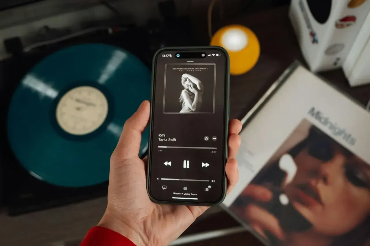 Mano che tiene uno smartphone con la copertina di un album di Taylor Swift. Accanto, un vinile blu e la copertina di "Midnights". Nonostante l'atmosfera moderna, si percepisce il fascino delle canzoni sudamericane.
