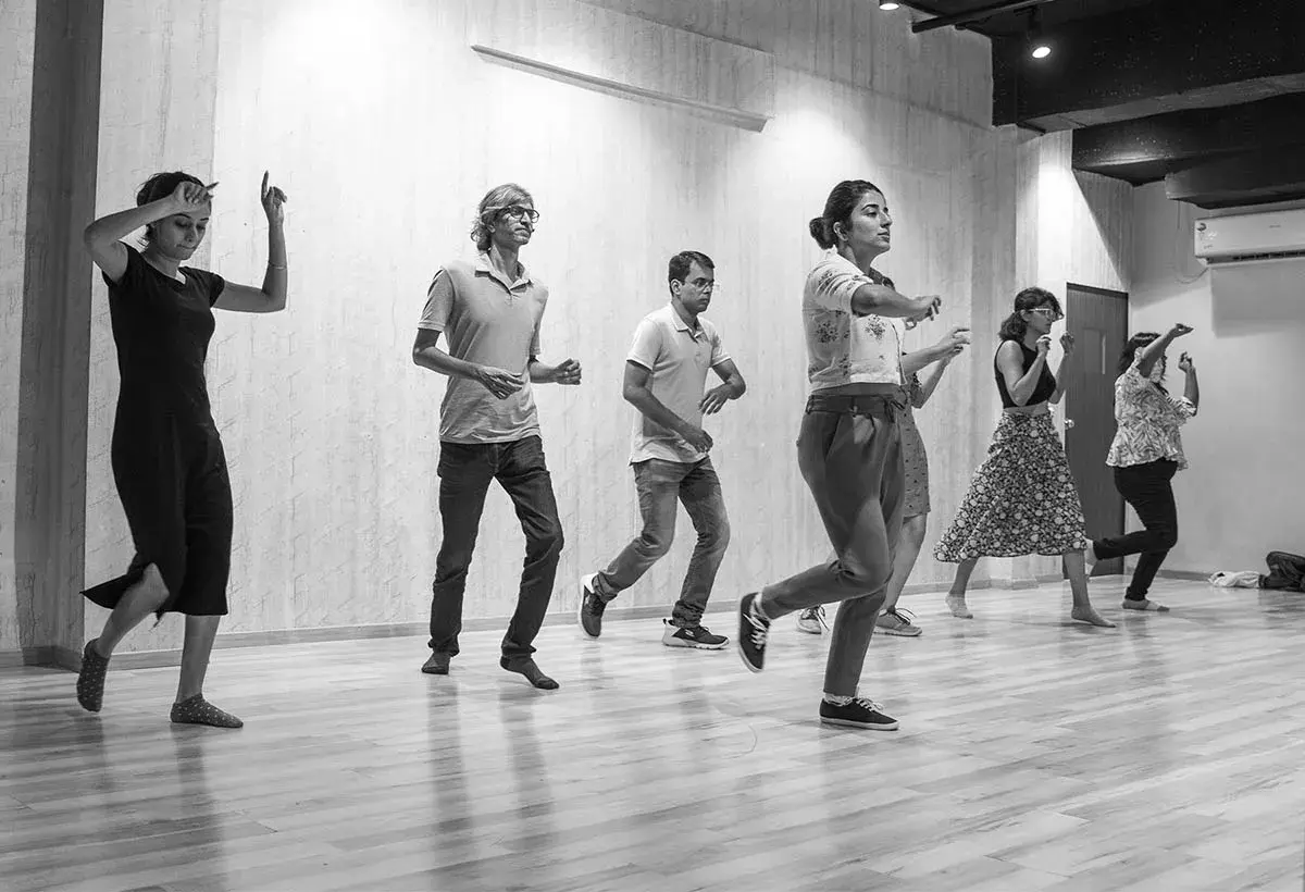 Un gruppo di persone impara come si balla lo swing in una sala prove. Movimenti energici e sorrisi contagiosi.