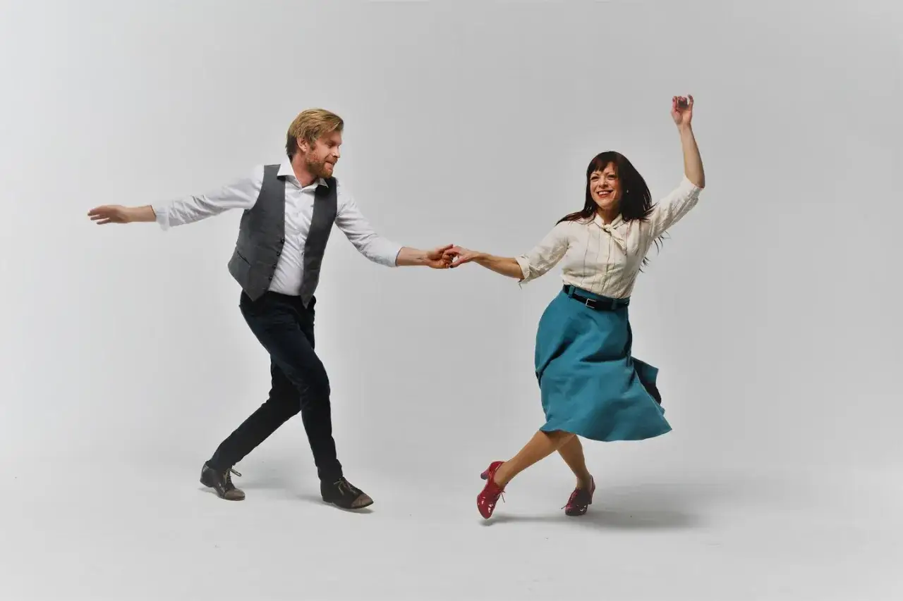 Coppia balla swing, uomo con gilet e donna con gonna svolazzante. La differenza tra swing e lindy hop è evidente nel loro dinamismo.