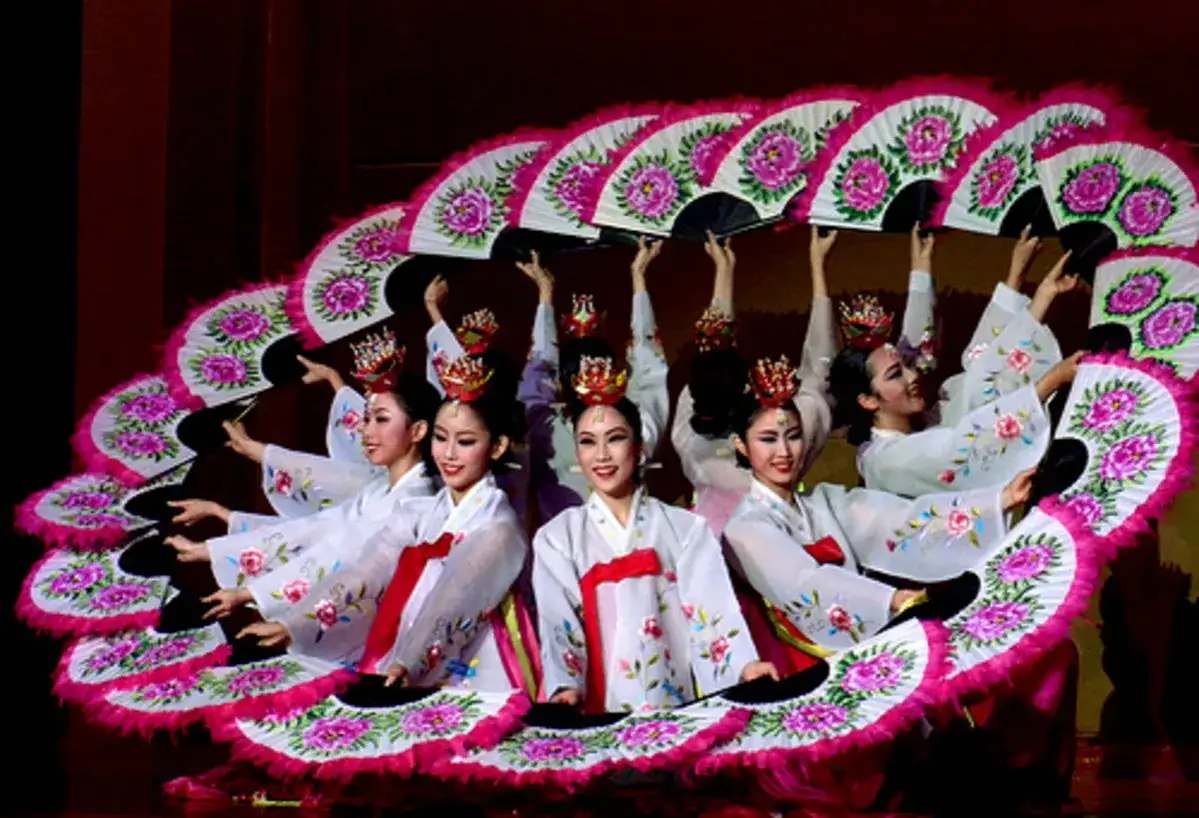 Donne in abiti tradizionali coreani eseguono una danza con ventagli decorati, creando un effetto a ventaglio.