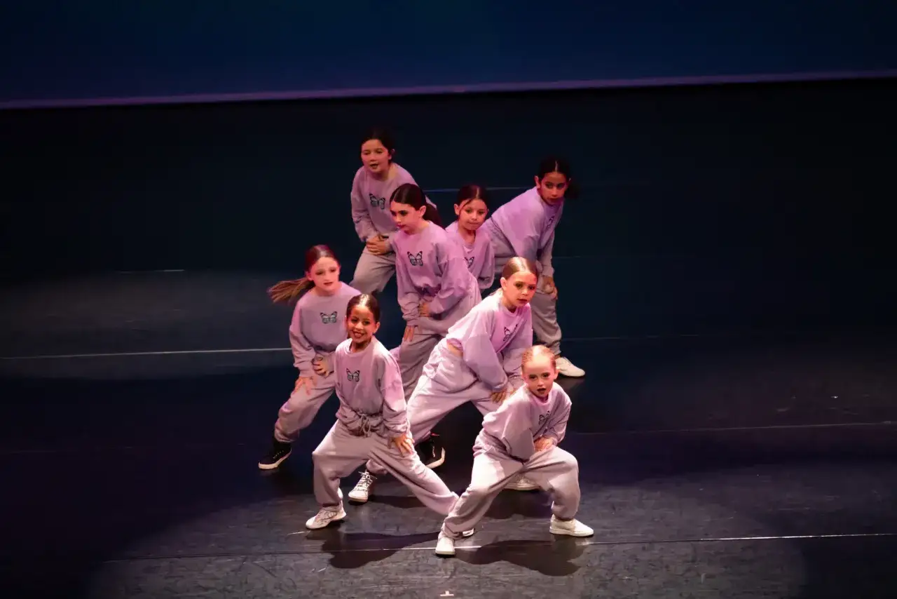 Un gruppo di bambine in tenuta sportiva viola esegue un ipop ballo sul palco, con espressioni concentrate e movimenti sincronizzati.