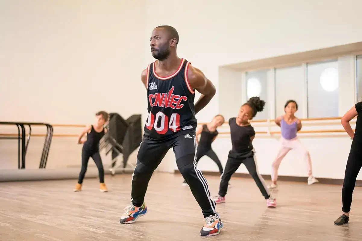 Un uomo guida un gruppo di bambini in una lezione di danza moderna hip hop in uno studio luminoso.
