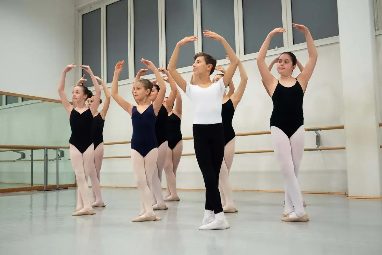 Giovani ballerini in una lezione di danza classica, con le braccia alzate in un esercizio.