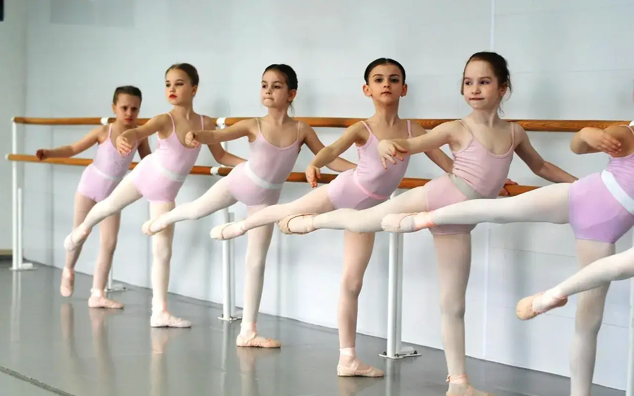 Bambine in tut&ugrave; rosa praticano la danza propedeutica alla sbarra, con le gambe tese e i piedi in punta.