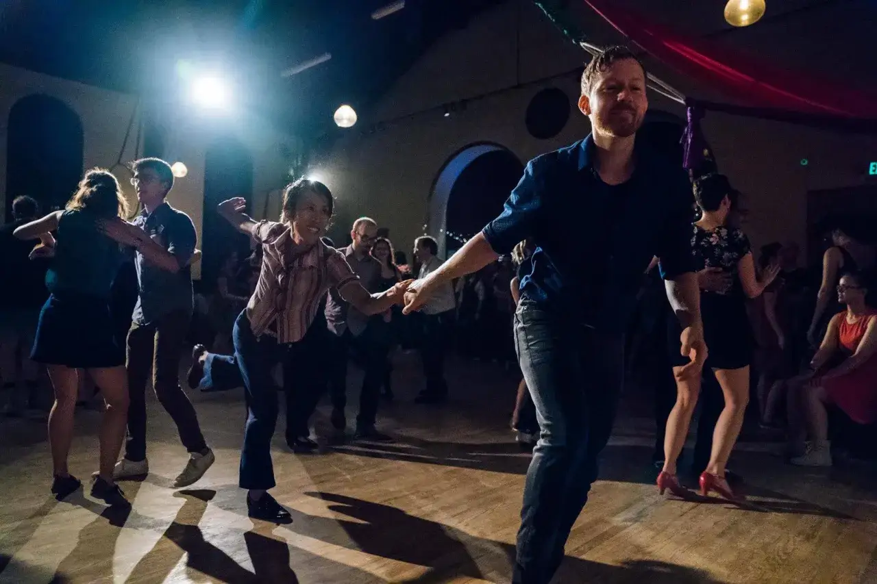 Coppie danzano con gioia in una scuola di ballo swing, con luci soffuse e un'atmosfera vivace.