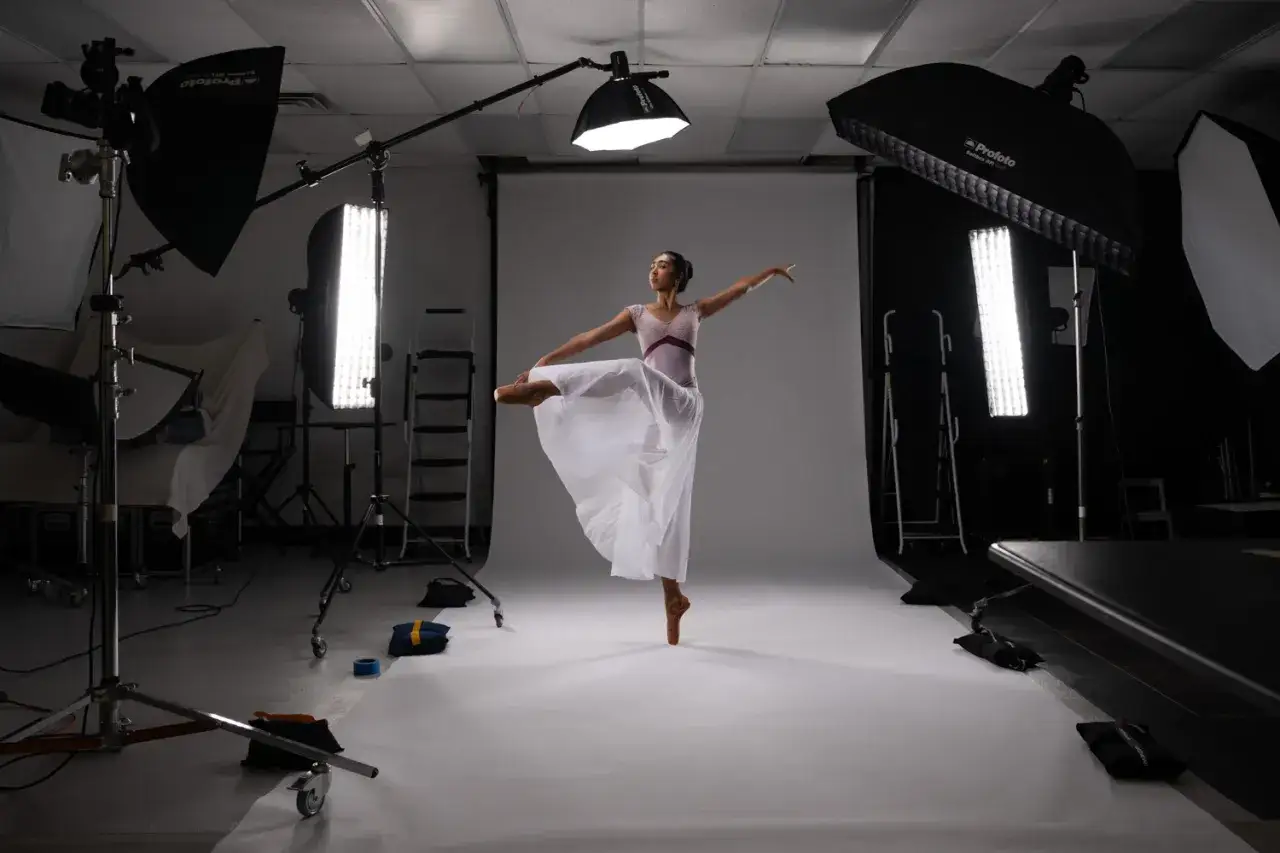 Una ballerina in posa in uno studio fotografico, circondata da luci e attrezzature. Questo &egrave; un esempio di come creare un video dance.