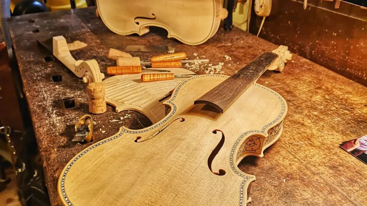 Il liutaio, con la sua arte, d&agrave; forma a strumenti musicali. In laboratorio, un violino in costruzione, con legni grezzi e attrezzi.