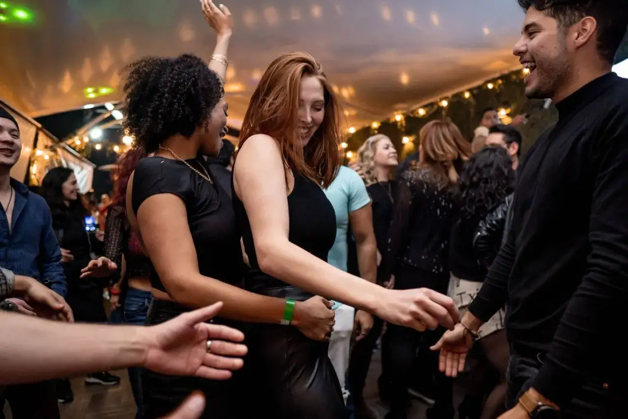 Giovani ballano con gioia in un evento che ricorda le scuole latino americano, con luci soffuse e un'atmosfera festosa.