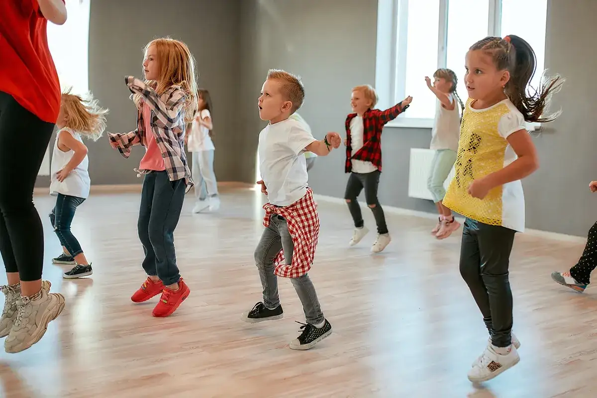 Bambini entusiasti partecipano a corsi hip hop, muovendosi a ritmo con gioia in una sala luminosa.