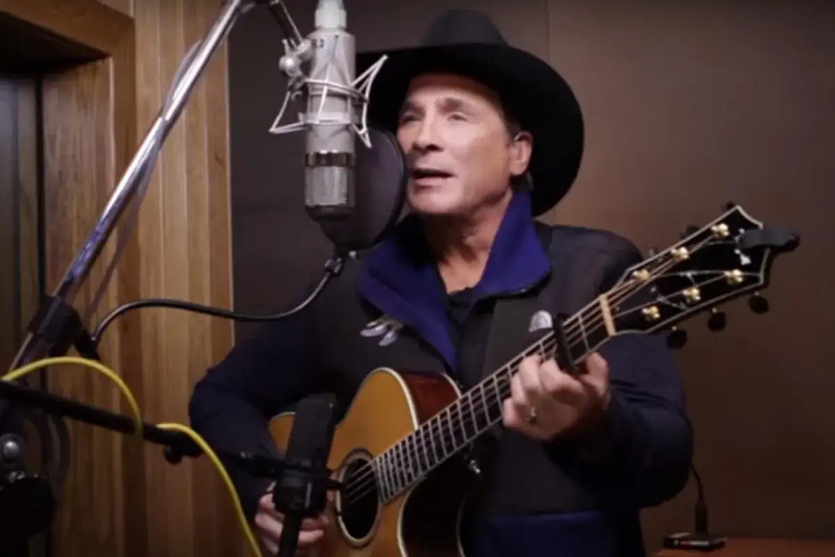 Cantante con cappello da cowboy e chitarra acustica in studio, pronto a registrare canzoni country famose.