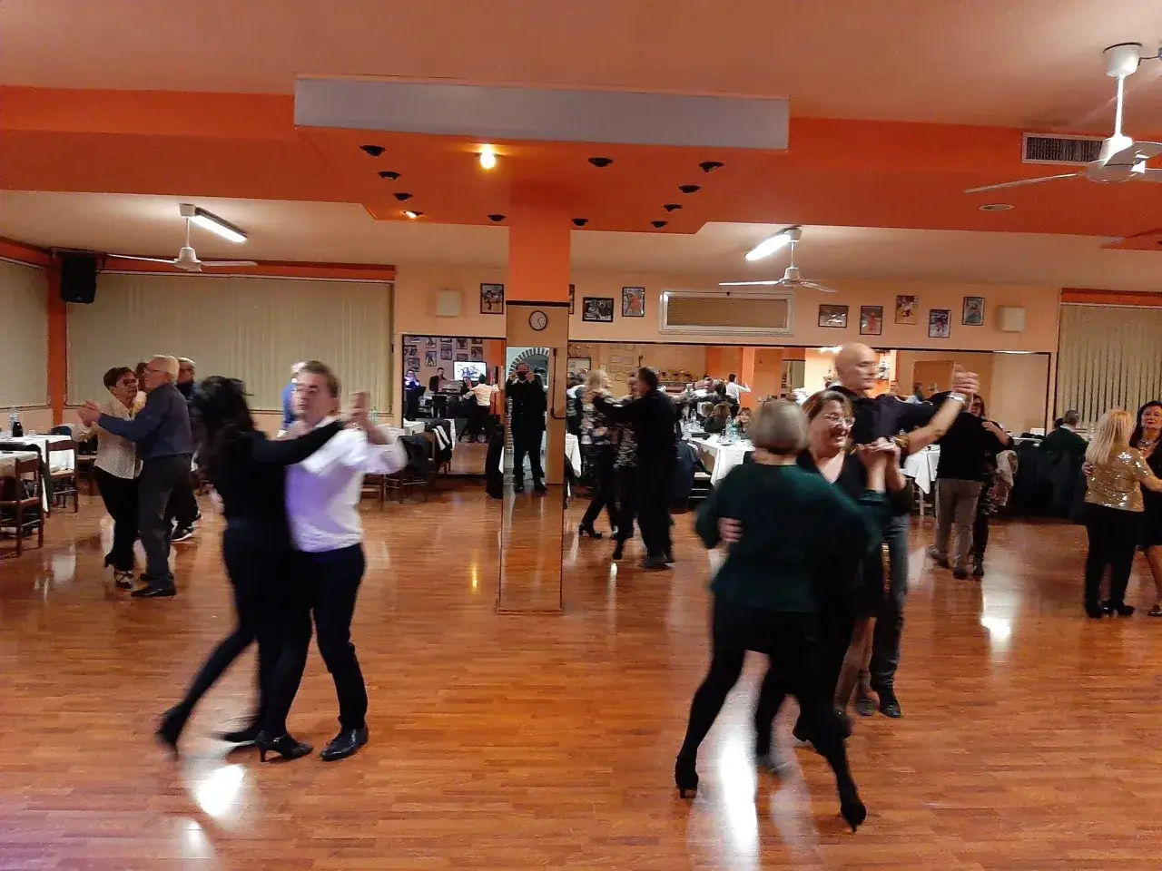 Coppie danzano in una sala con pavimento in legno lucido, un'atmosfera vivace che ricorda i salti di quando si va a ballare.