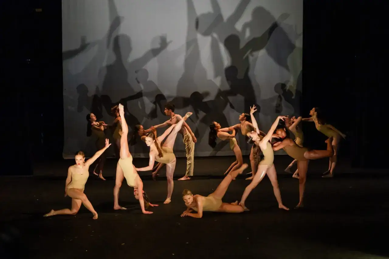 Giovani ballerini in scena, in pose dinamiche e aggraziate, durante i corsi di danza moderna. Le ombre sullo sfondo amplificano l'effetto scenico.