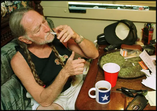 Willie Nelson, icona delle canzoni country famose, si accende una sigaretta con una tazza di caffè accanto.